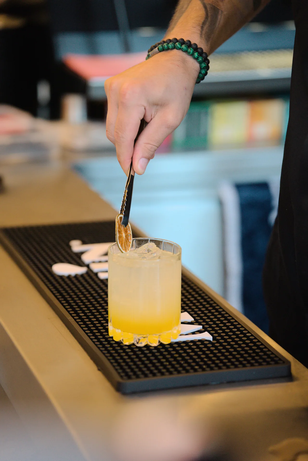 Eine Hand garniert einen gelben Cocktail an der Bar