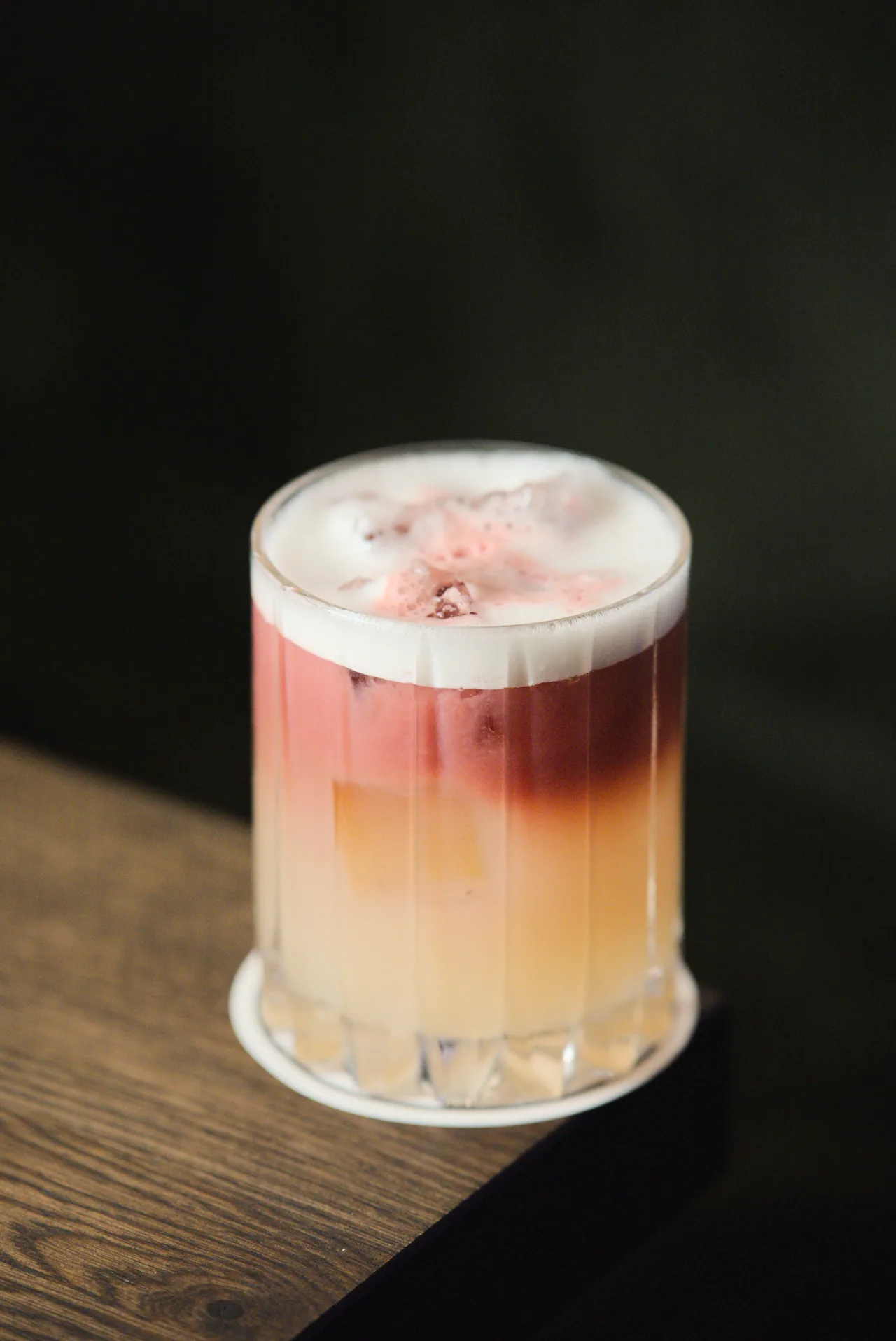 Cocktail mit gelb-violettem Farbverlauf und Schaum auf einem Holztisch